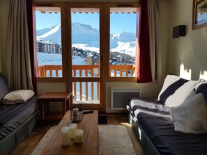 A cozy room with a bed, a sofa, a wooden table with candles, and a view of snow-covered mountains. - Plagne Soleil Appart for 5 persons PIED DES PISTES /PLEIN SUD (Mâcot-la-Plagne)