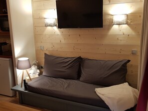 A cozy room with a bed, a TV mounted on the wall, and a lamp on a bedside table. - Plagne Soleil Appart for 5 persons PIED DES PISTES /PLEIN SUD (Mâcot-la-Plagne)