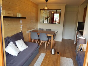 A cozy living room with a sofa, dining table, and chairs. A mirror hangs above the table, and a lamp is on the right. - Plagne Soleil Appart for 5 persons PIED DES PISTES /PLEIN SUD (Mâcot-la-Plagne)