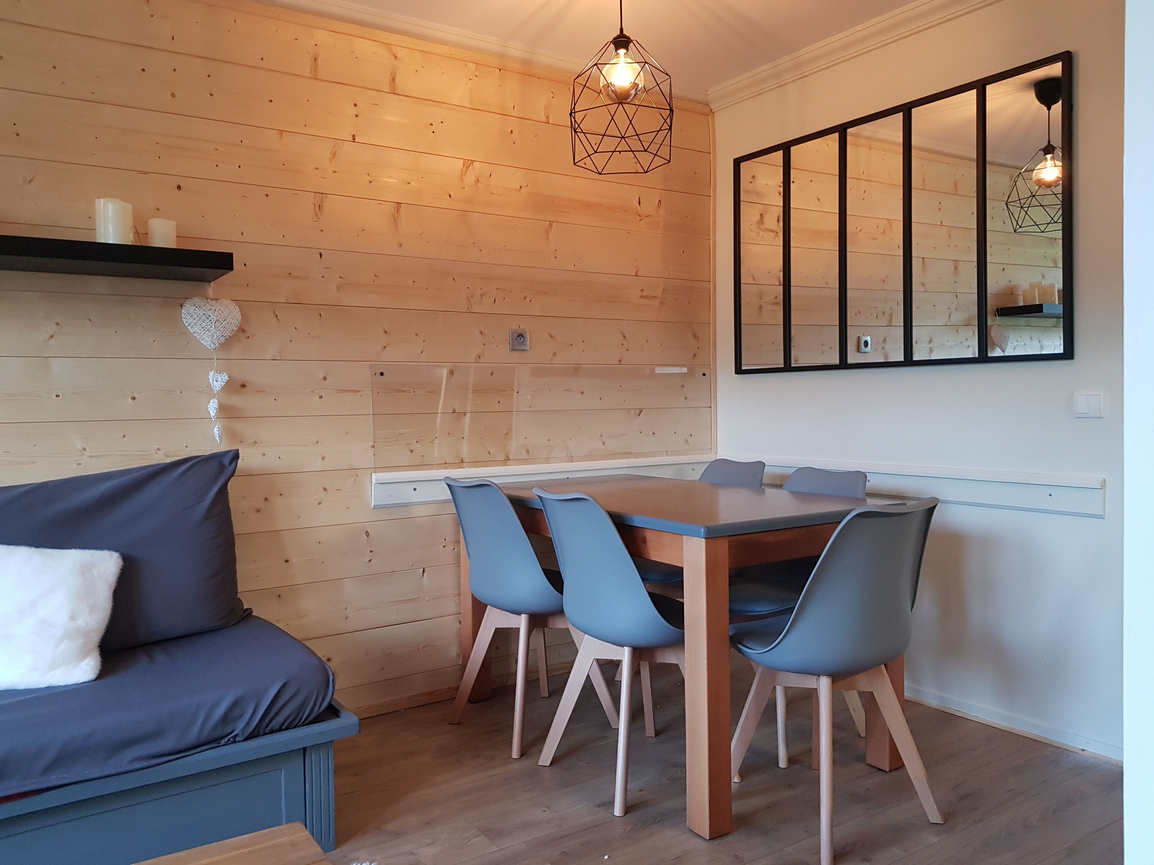 Un espace de repas moderne avec un mur en bois, une table à manger avec des chaises, un canapé et un luminaire suspendu.