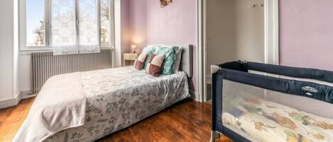 A bedroom with a bed, a crib, a radiator, and a window with a view.