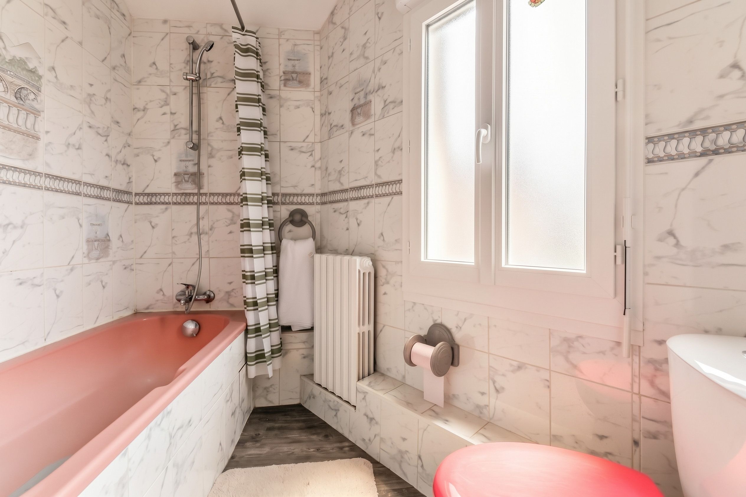 Une salle de bain avec un mur en marbre, une baignoire, des toilettes, une douche et une fenêtre.