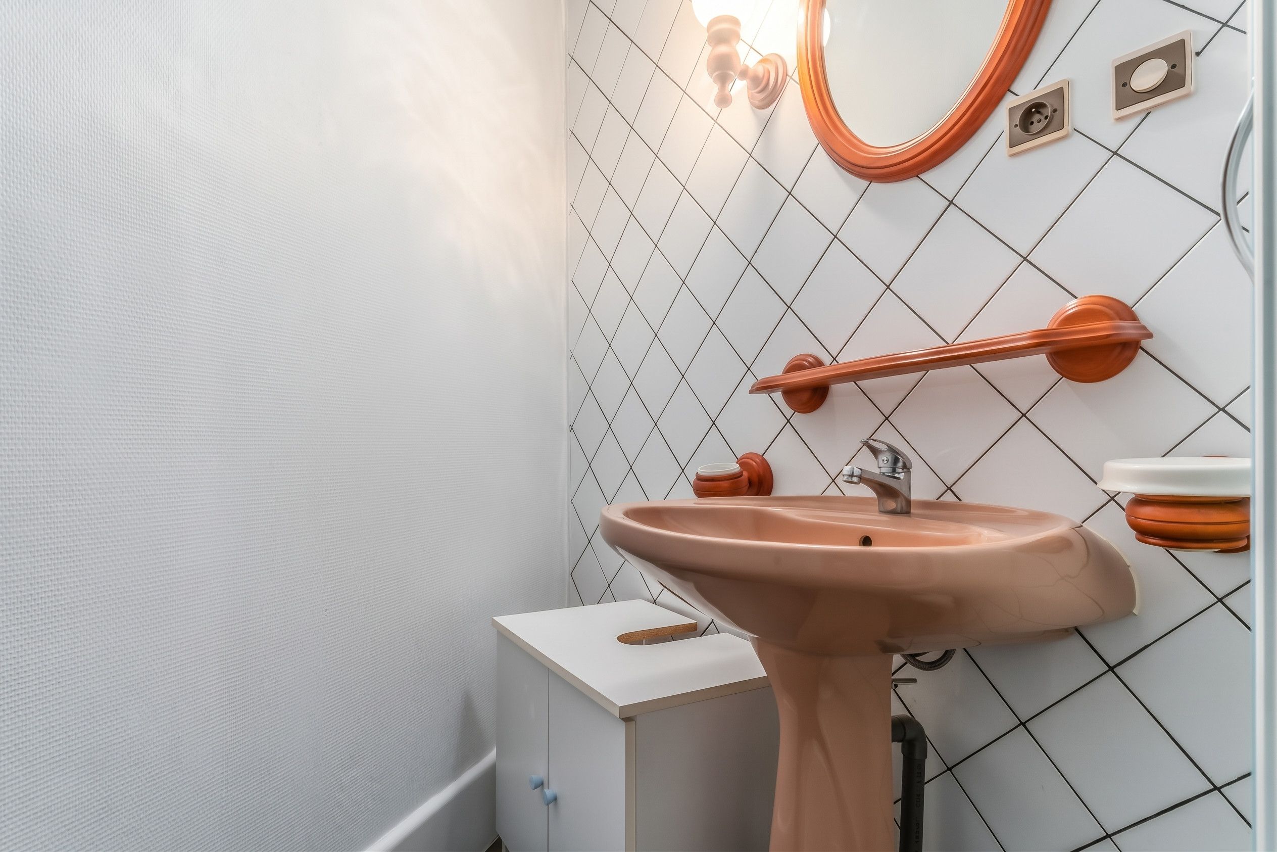 Une salle de bain avec un lavabo blanc, un miroir et un mur recouvert de carreaux.