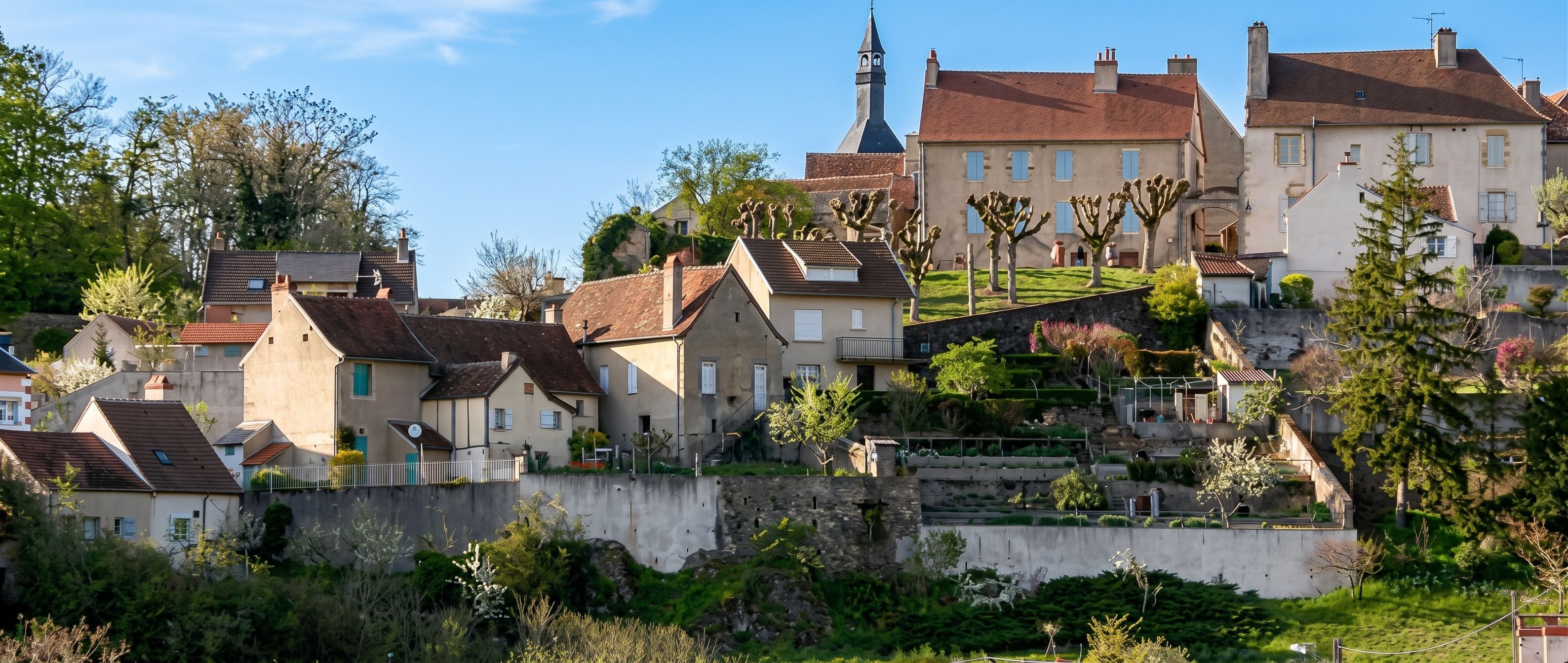 A hillside residential area with houses, a church, and a stone wall.