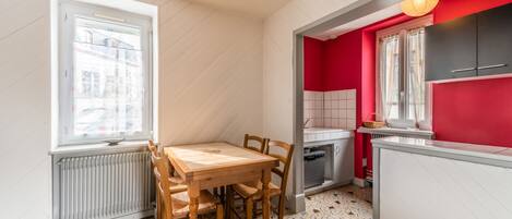 Une cuisine compacte avec une table et des chaises, un mur d’accent rouge et une vue par la fenêtre.
