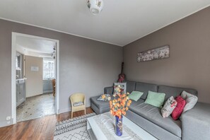 Un salon avec un canapé gris, un fauteuil en osier, une table basse et un vase rempli de fleurs oranges.