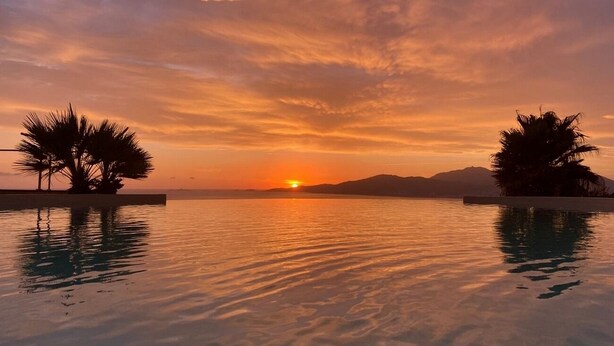 Un coucher de soleil sur un étang paisible, bordé de palmiers de chaque côté.
