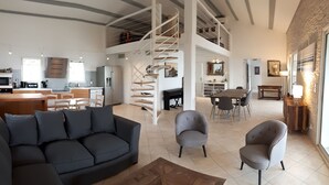 Un vaste espace de vie comprenant une cuisine moderne, un coin repas et une chambre en mezzanine accessible par un escalier en colimaçon.