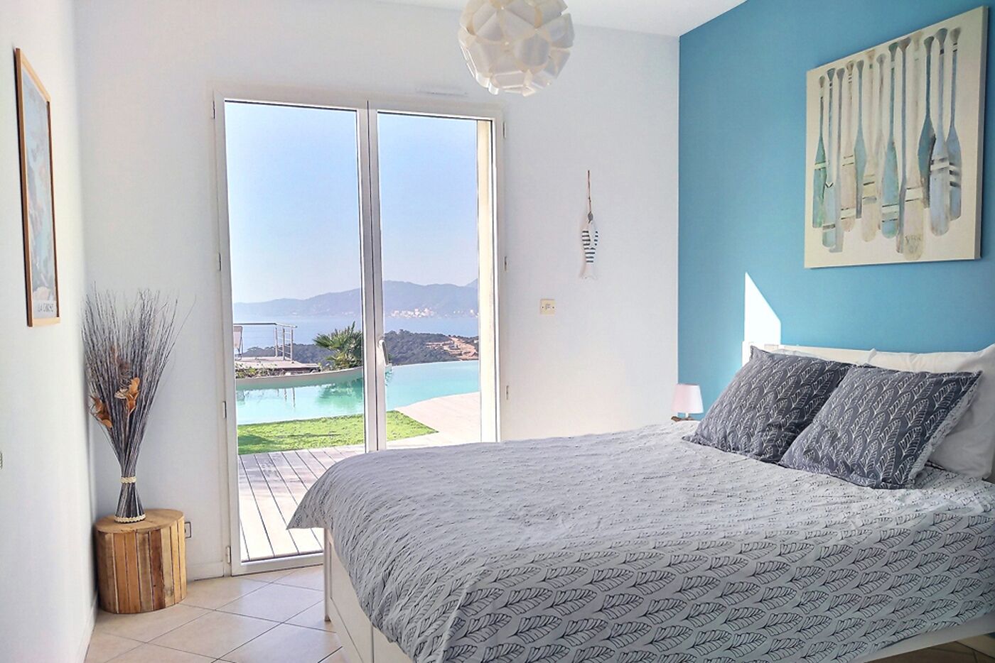 A bedroom with a bed, a view of a pool and mountains, and a painting on the wall.