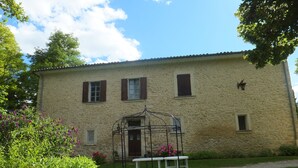 A two-story stone building with a balcony, a small garden with a bench, and a clear blue sky. - In a mansion of the nineteenth century, cottage for 5 people (forcalquier)
