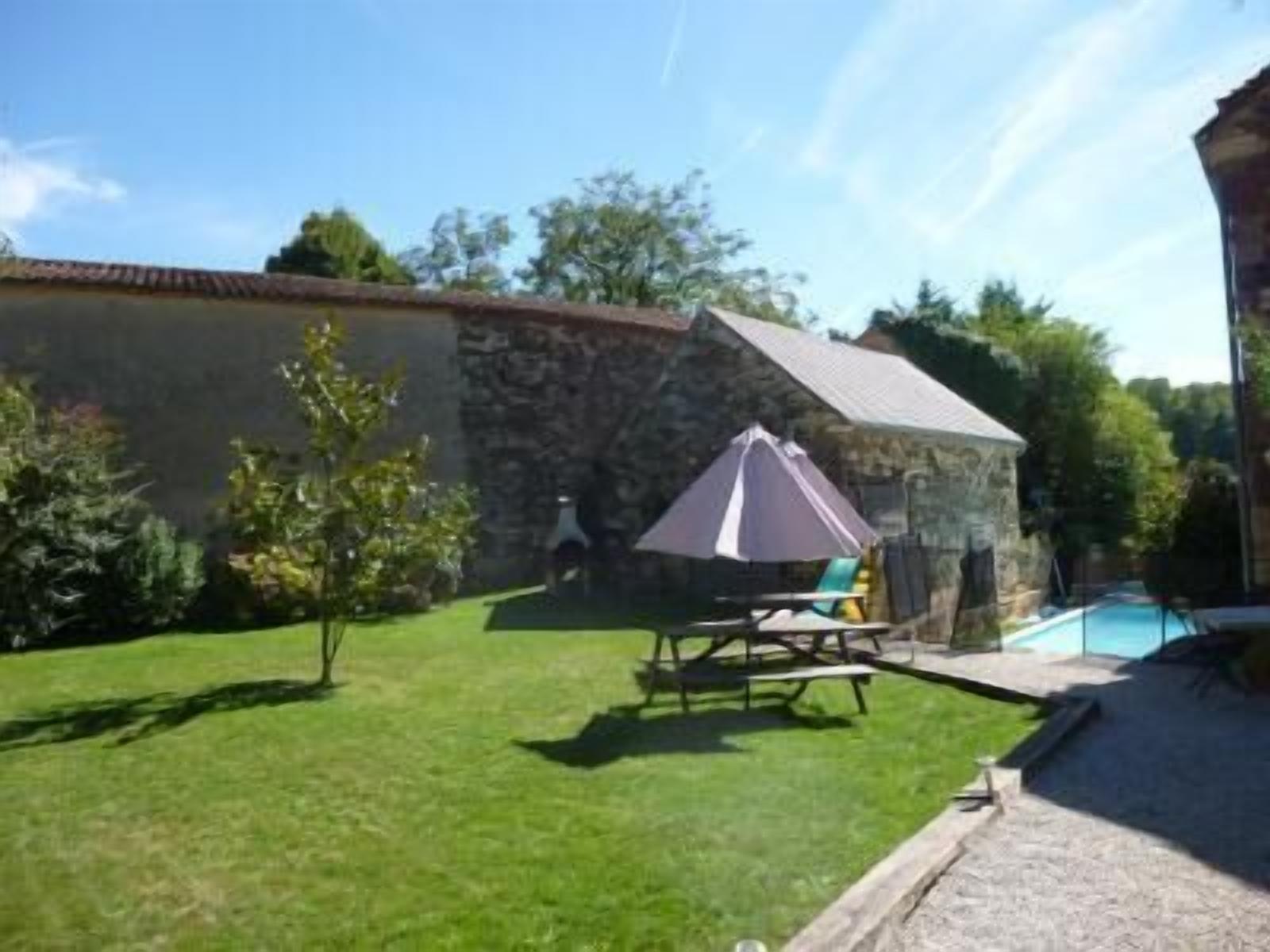 A stone building with a swimming pool, a grassy lawn, and a patio area with a table and chairs.