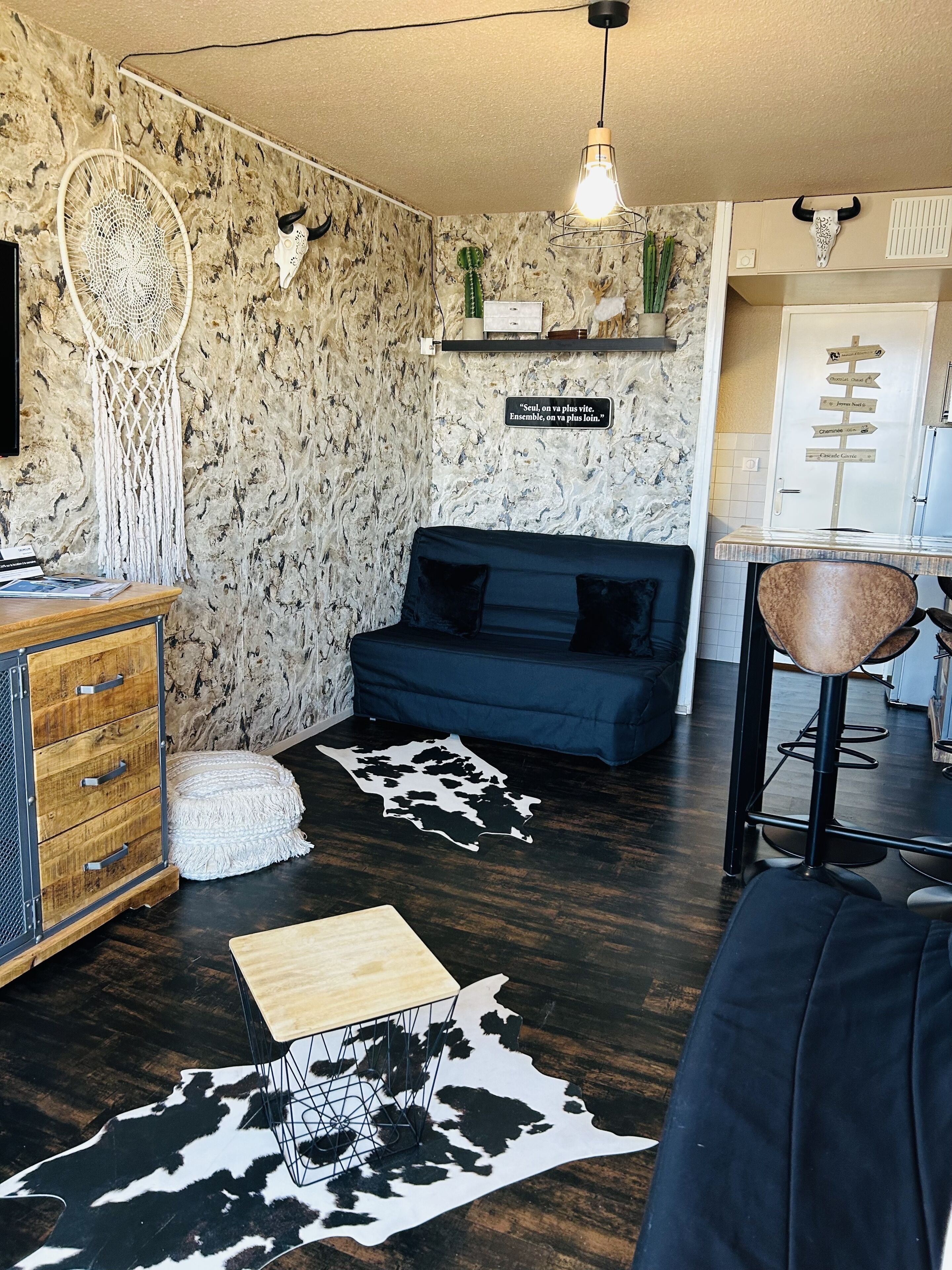A living room with a dark blue sofa, a wooden coffee table, a cowhide rug, a macrame wall hanging, and a wall-mounted cactus.