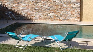 Una piscina con dos sillas reclinables turquesa y un muro de piedra al fondo.