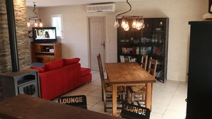 Una sala de estar acogedora con un sofá rojo, una mesa de comedor de madera y un televisor. Hay estanterías y una chimenea.