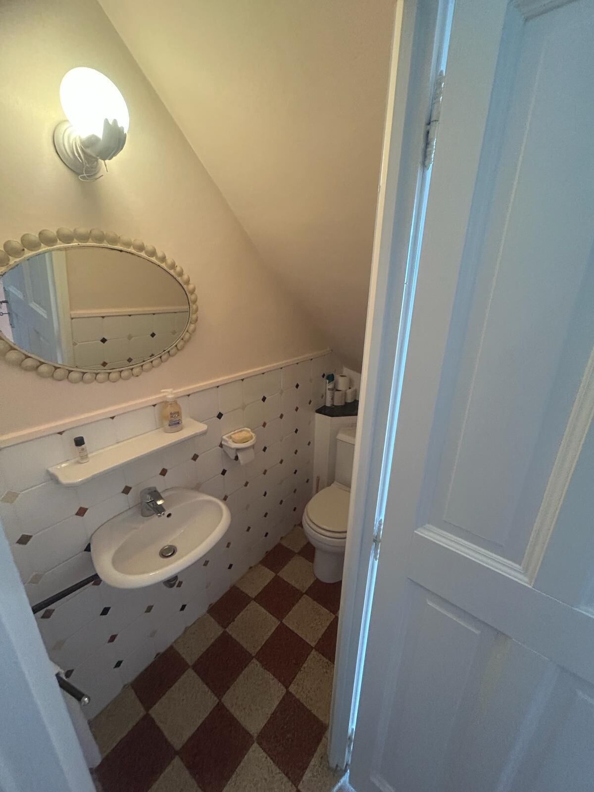 Une petite salle de bain avec un lavabo blanc, un miroir et des toilettes. Le sol est recouvert d’un carrelage à motifs géométriques, et un porte-serviettes est fixé au-dessus du lavabo.