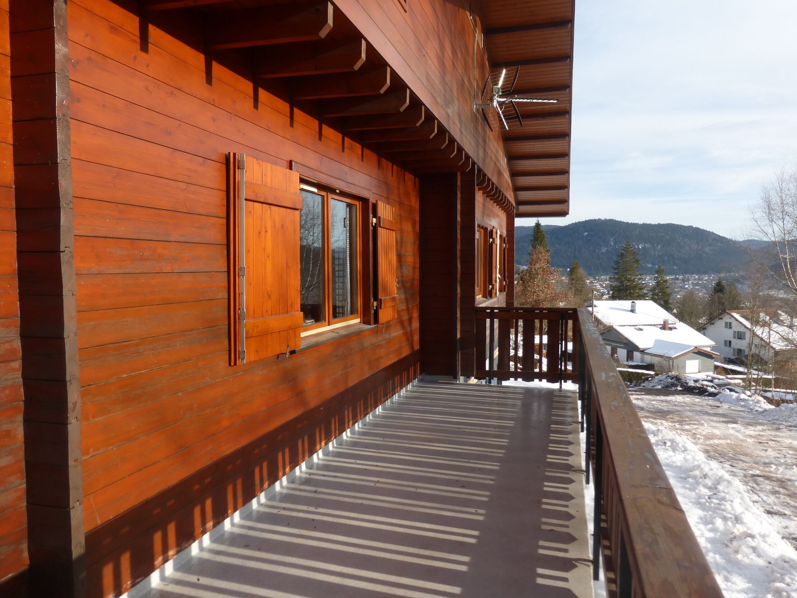 Un bâtiment en bois doté d’un balcon donnant sur un paysage enneigé et des montagnes lointaines.