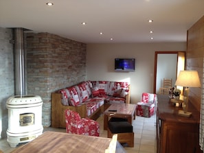 A cozy living room with a stone wall, a white stove, a red and white patterned sofa, a wooden coffee table, and a television mounted on the wall. - NEW: GERARDMER Mountain chalet 12 people (Gérardmer)