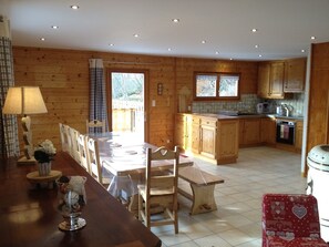 A wooden cabin-style kitchen with a dining area, featuring a large table, chairs, and a red suitcase. - NEW: GERARDMER Mountain chalet 12 people (Gérardmer)