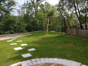 A backyard with a wooden swing set, a stone pathway, and a wooden deck. - NEW: GERARDMER Mountain chalet 12 people (Gérardmer)
