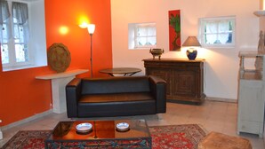 A living room with a black sofa, a wooden coffee table, a red rug, a cabinet, and a lamp. - Cottage with a pond on the border of Brittany and Normandy (La Baconnière)