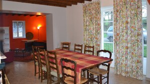 A dining area with a wooden table and chairs, a red and orange tablecloth, and a lamp. - Cottage with a pond on the border of Brittany and Normandy (La Baconnière)