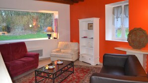 A living room with a red couch, a white armchair, a black leather sofa, a glass coffee table, and a white shelving unit. - Cottage with a pond on the border of Brittany and Normandy (La Baconnière)
