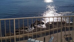 Een balkon met uitzicht op zee, een hekwerk en enkele stoelen.