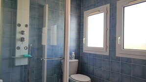 Een badkamer met blauwe tegels, een glazen douchecabine, een toilet en een raam.