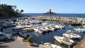 Un port de plaisance où sont amarrés de nombreux bateaux, une jetée en pierre et, au fond, une imposante tour rouge qui se distingue.