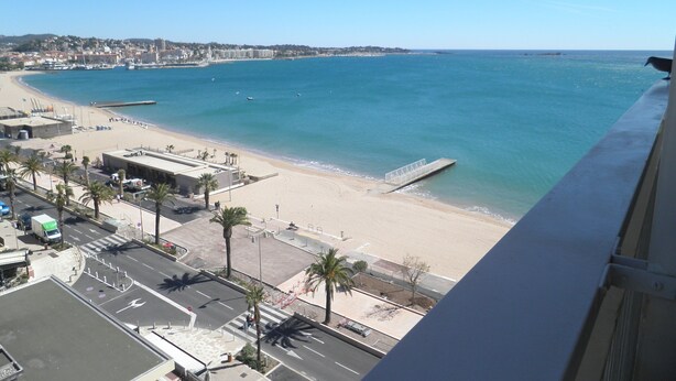 Un paysage urbain côtier avec une plage, une jetée et une route menant à un bâtiment doté d’un parking.