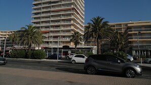 Un hôtel à plusieurs étages, doté de balcons, de palmiers et donnant sur une rue bordée de voitures garées.