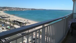Un balcon avec vue sur une plage et l’océan, un parking et des bâtiments situés au loin.