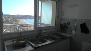 Une cuisine dotée d’une grande fenêtre, d’un évier et offrant une vue sur une plage et le paysage urbain.