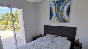 A bedroom with a bed, a ceiling light, a painting, and a view of palm trees. - Vista Para o Mar, Calmo / sem Vis-à-vis, a 5min da Praia, Piscina com Portões (Calvi)