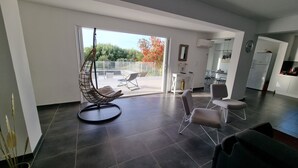A modern living room with a hanging chair, a dining area, and a kitchen. - Vista Para o Mar, Calmo / sem Vis-à-vis, a 5min da Praia, Piscina com Portões (Calvi)