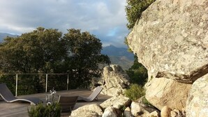 Eine Holzterrasse mit Liegestühlen, umgeben von Steinen und Pflanzen, mit Blick auf eine Berglandschaft.