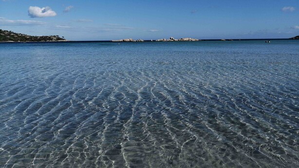 Ein klarer Blick auf ein ruhiges Meer mit einer felsigen Küste im Hintergrund.