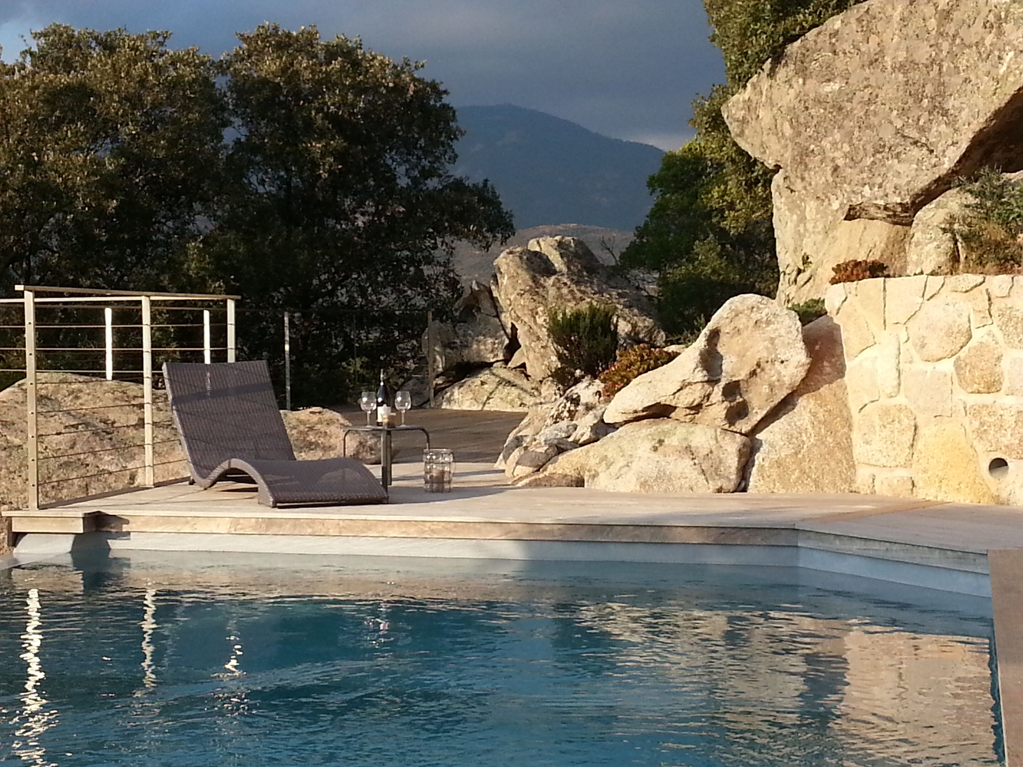 A pool area with a lounge chair, a stone wall, and a view of mountains.