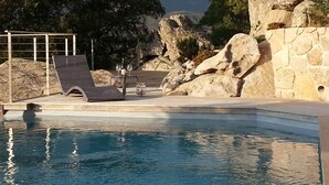 Ein Poolbereich mit Liegestuhl, einer Steinsäule und Blick auf Berge.