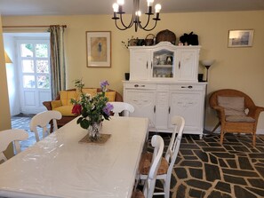 A dining area with a white table, chairs, a vase with flowers, a white cabinet, and a wicker chair.