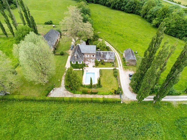 Eine Vogelperspektive zeigt ein großes Anwesen mit einem Haupthaus, einem Swimmingpool und umliegenden grünen Feldern.