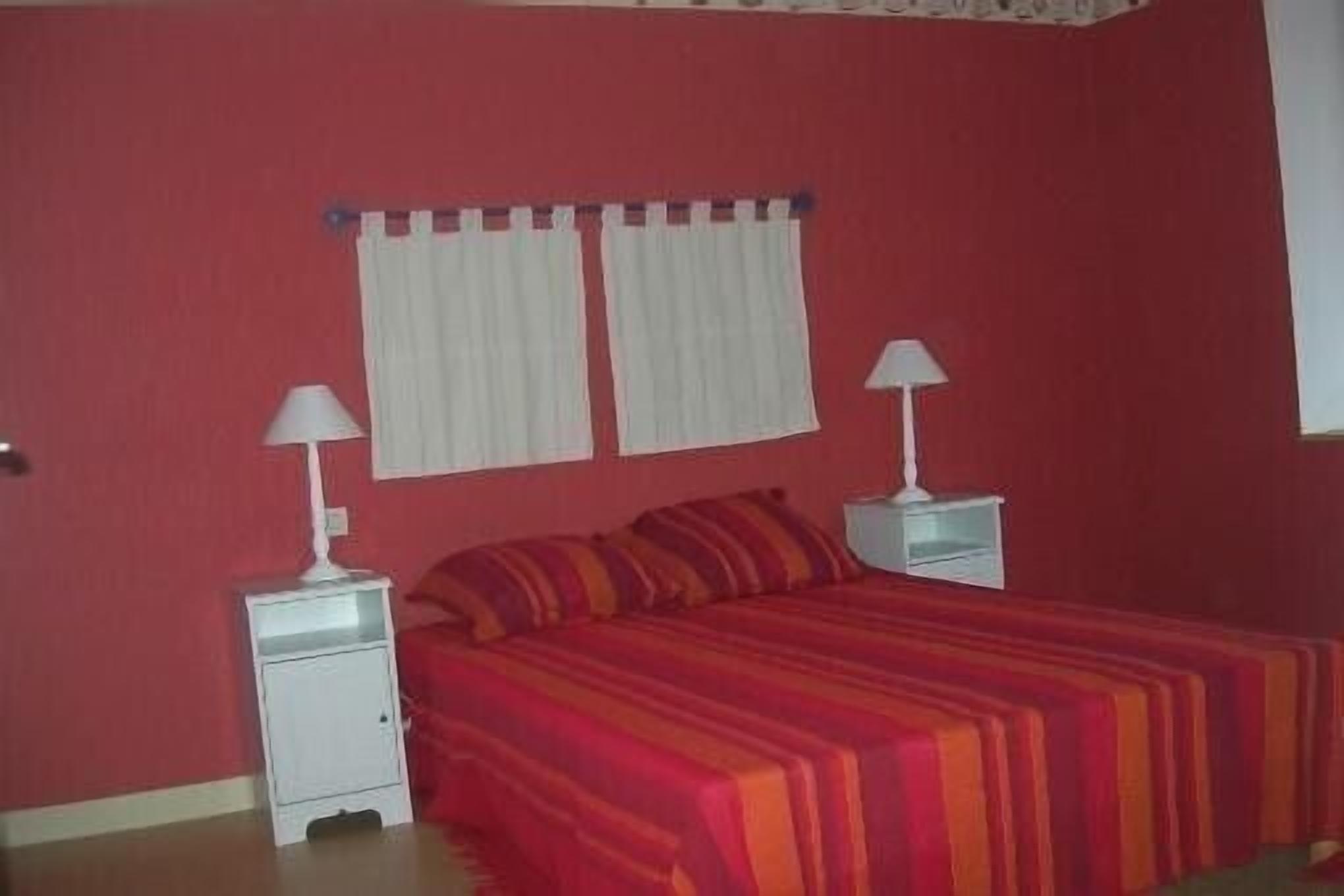 Een slaapkamer met een bed, twee nachtkastjes met lampen, en een raam met gordijnen.