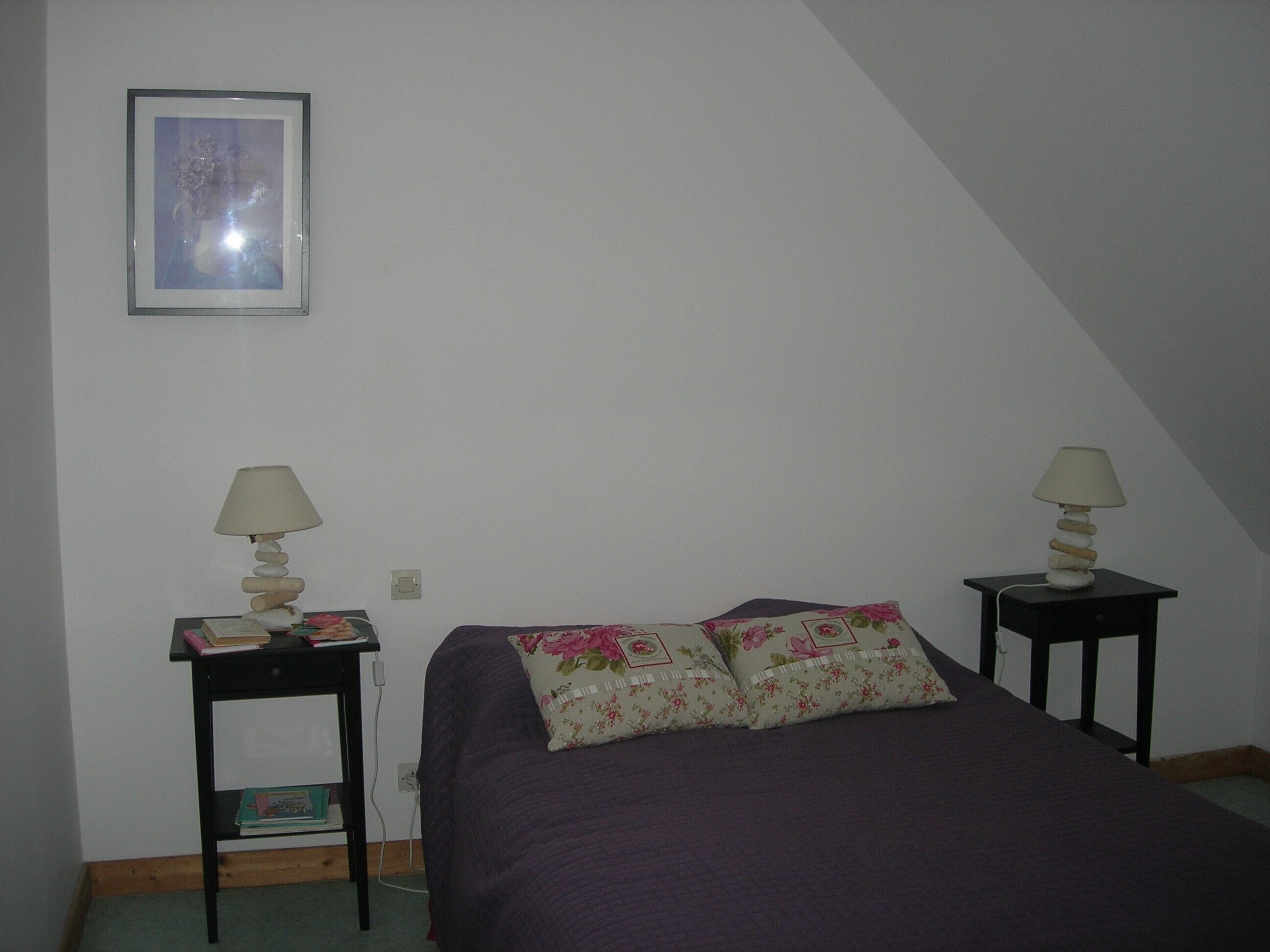 Una camera da letto con un letto, due comodini, un tavolino e un quadro appeso al muro, oltre a una finestra.