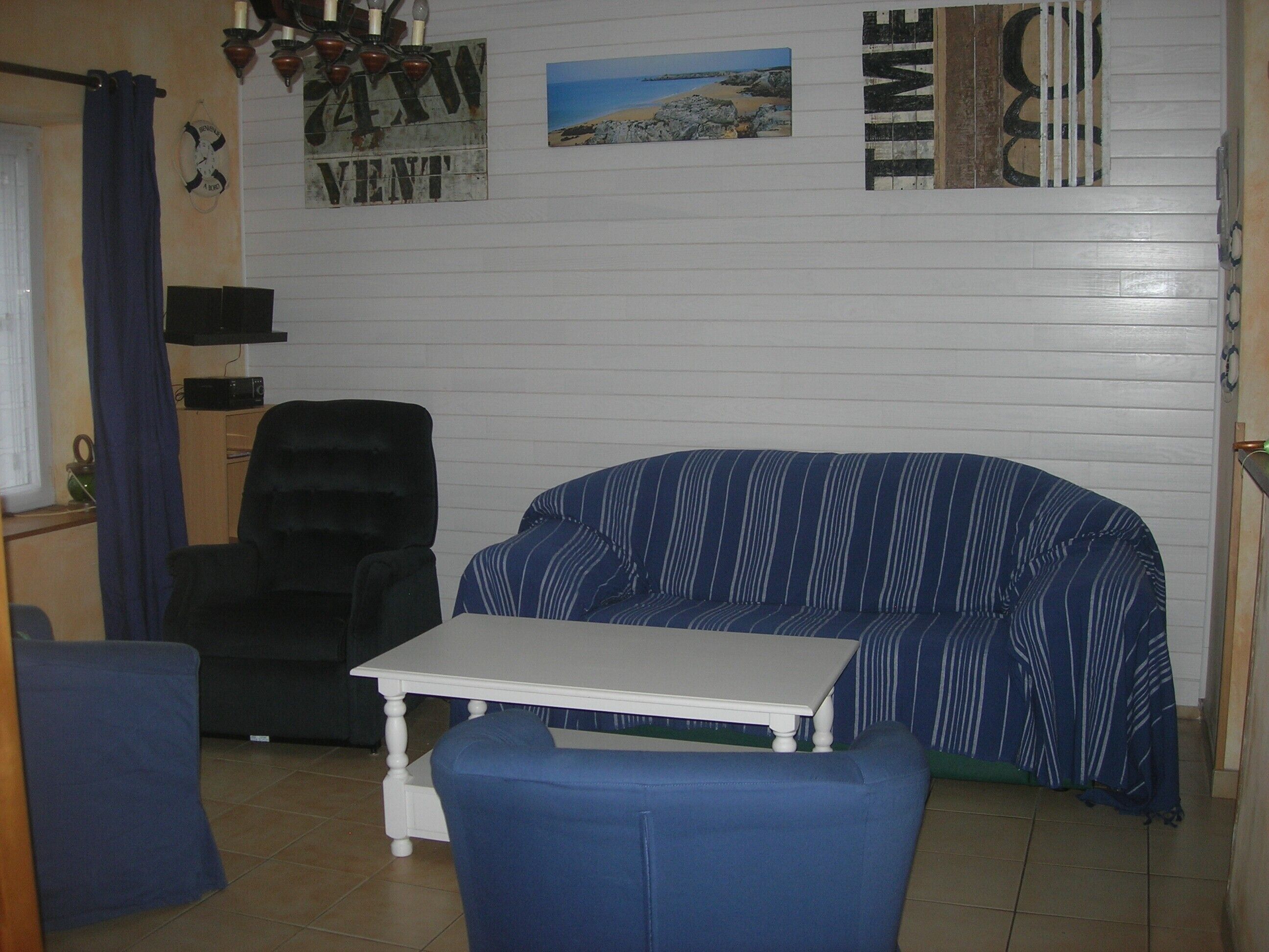 A room with a striped sofa, a small table, a black chair, and a wall with a clock and a poster.