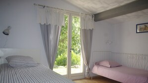 A bedroom with two beds, a window with curtains, a radiator, and a picture on the wall.
