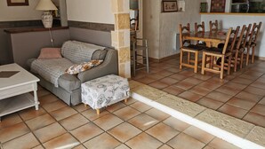 A cozy living area with a sofa, a small table, a dining table with chairs, and a kitchen area with a stove and shelves.