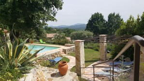 A pool area with a stone pathway, a terracotta pot, and lounge chairs.