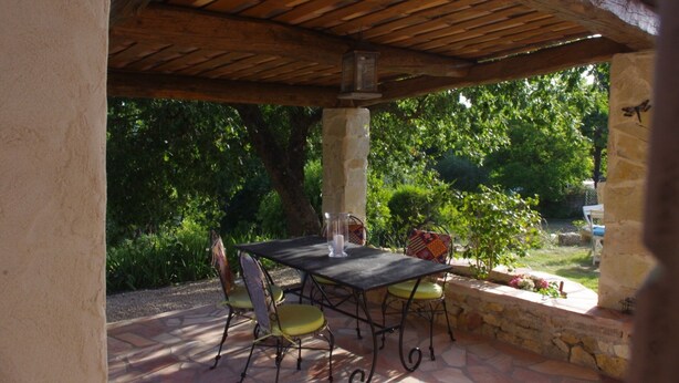 An outdoor patio with a table and chairs, surrounded by stone walls and greenery.