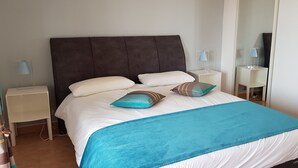 A neatly made bed with white bedding and a teal throw blanket. There are two bedside tables with lamps and a mirror. - Ste Maxime, sea view Comfortable, quiet, walk to the town center and beaches (Sainte-Maxime)
