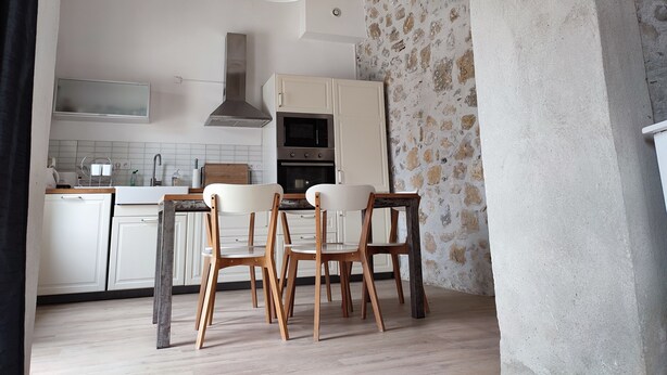 A modern kitchen with white cabinets, a built-in oven, and a stone accent wall. There are three wooden chairs and a hanging pendant light. - Stone house with Jacuzzi and air conditioning (Vallon-Pont-D'arc)
